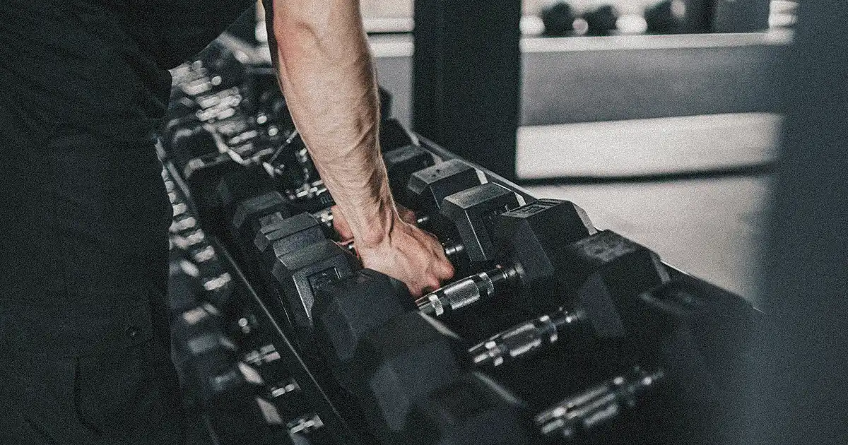 both hands grabbing dumbbells from the rack