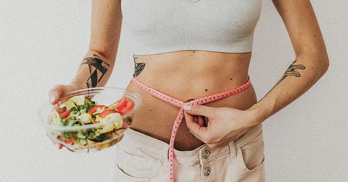 A woman holding a salad bowl and measuring her waist