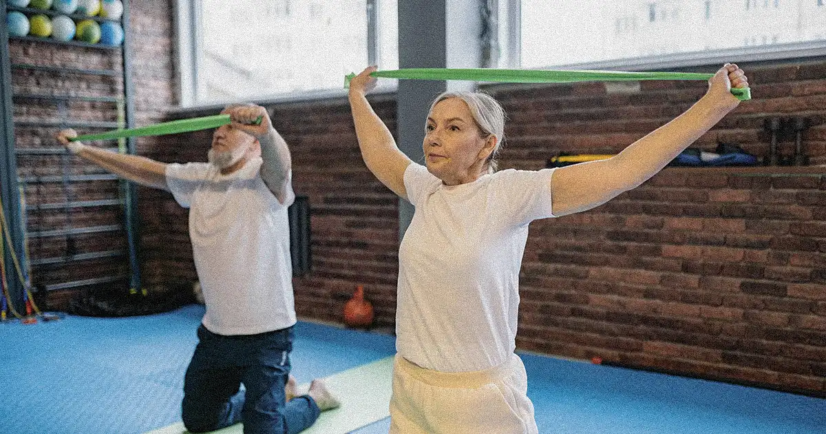 A woman and a man doing resistance band stretching on yoga mats in the gym